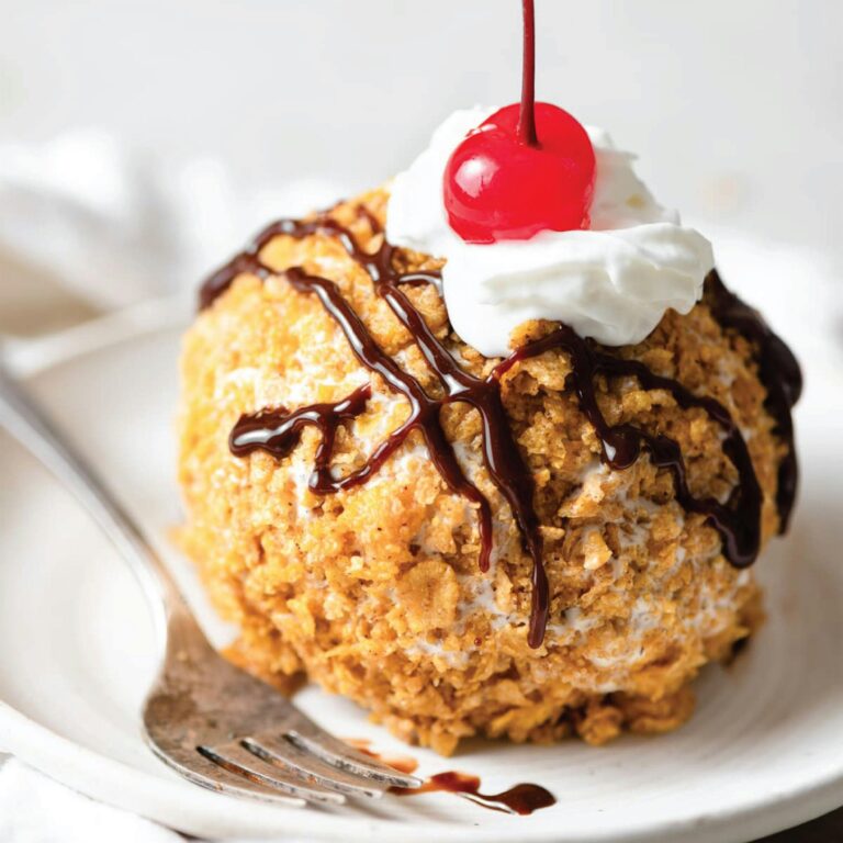 Close-up shot of a fried ice cream dessert with cherry, whipped cream, and chocolate syrup drizzles.